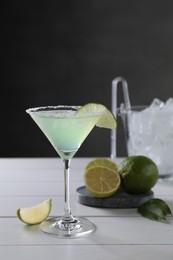 Photo of Delicious Margarita cocktail in glass and limes on white wooden table