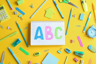 Photo of Small notebook with letters ABC and different school stationery on yellow background, flat lay