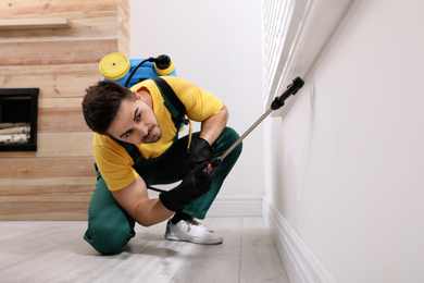 Pest control worker spraying insecticide on window sill at home