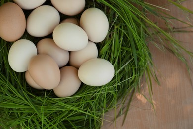 Photo of Nest made of green grass with fresh raw eggs on wooden table, top view