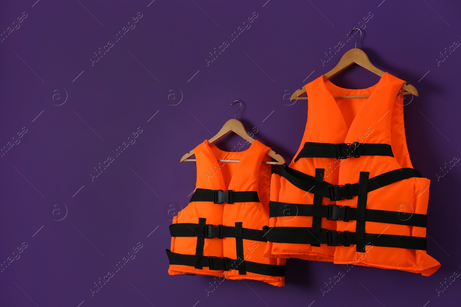 Photo of Orange life jackets on violet background. Space for text