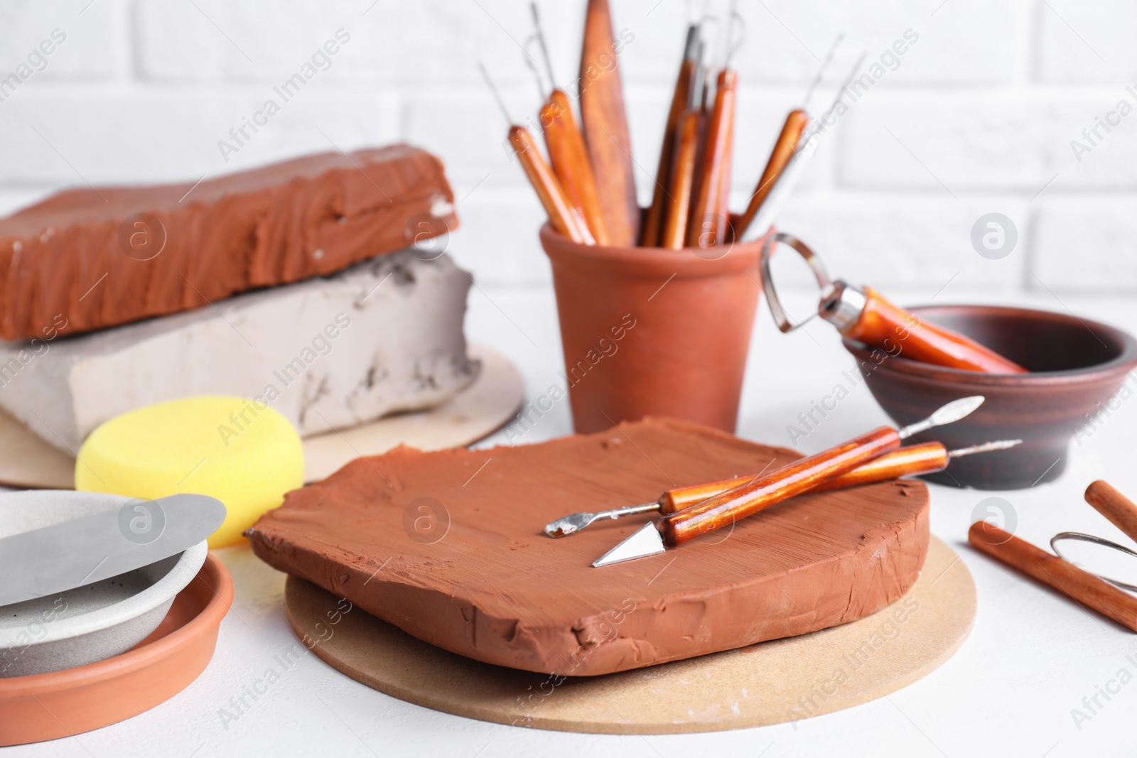 Photo of Clay and set of crafting tools on white textured table, closeup