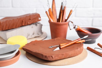 Clay and set of crafting tools on white textured table, closeup