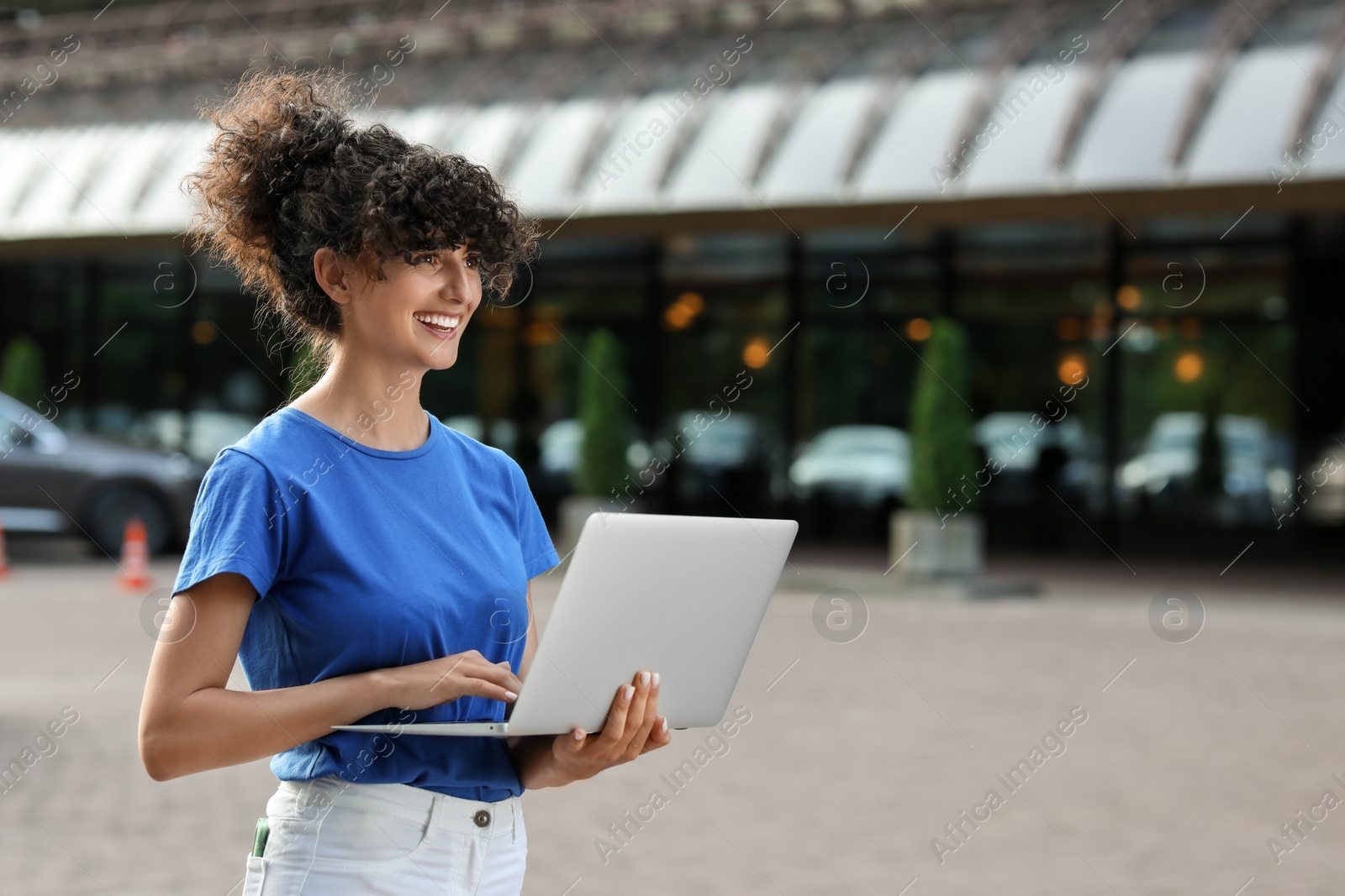 Photo of Happy young woman using modern laptop on city street. Space for text