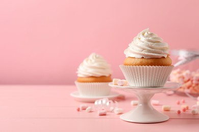 Delicious cupcakes decorated with cream on pink wooden table, space for text