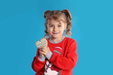 Cute little girl with Christmas gingerbread cookie on light blue background