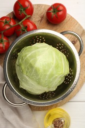 Photo of Wet cabbage in colander, oil and tomatoes on white wooden table, top view