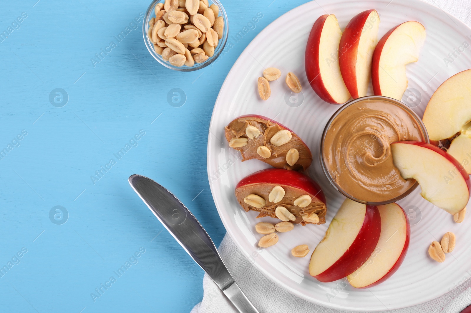 Photo of Slices of fresh apple with peanut butter, nuts and knife on light blue wooden table, flat lay. Space for text