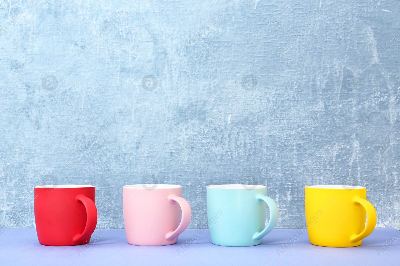 Photo of Different colorful cups on table against color background