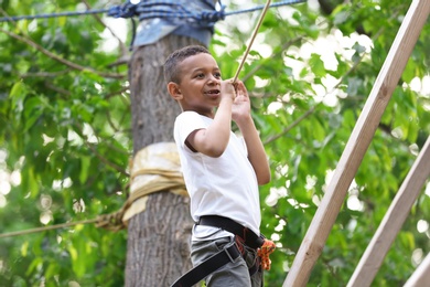 Little African-American boy climbing in adventure park. Summer camp