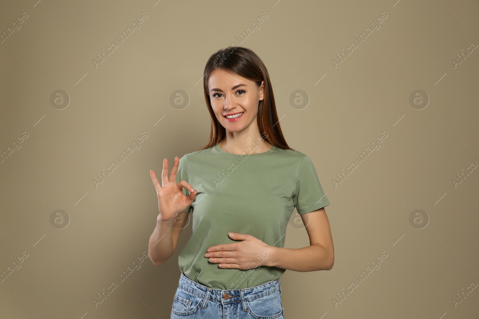 Photo of Healthy woman holding hand on belly and showing OK gesture against beige background