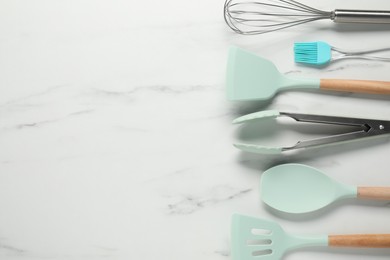 Photo of Different spatulas and other kitchen utensils on light marble table, flat lay. Space for text