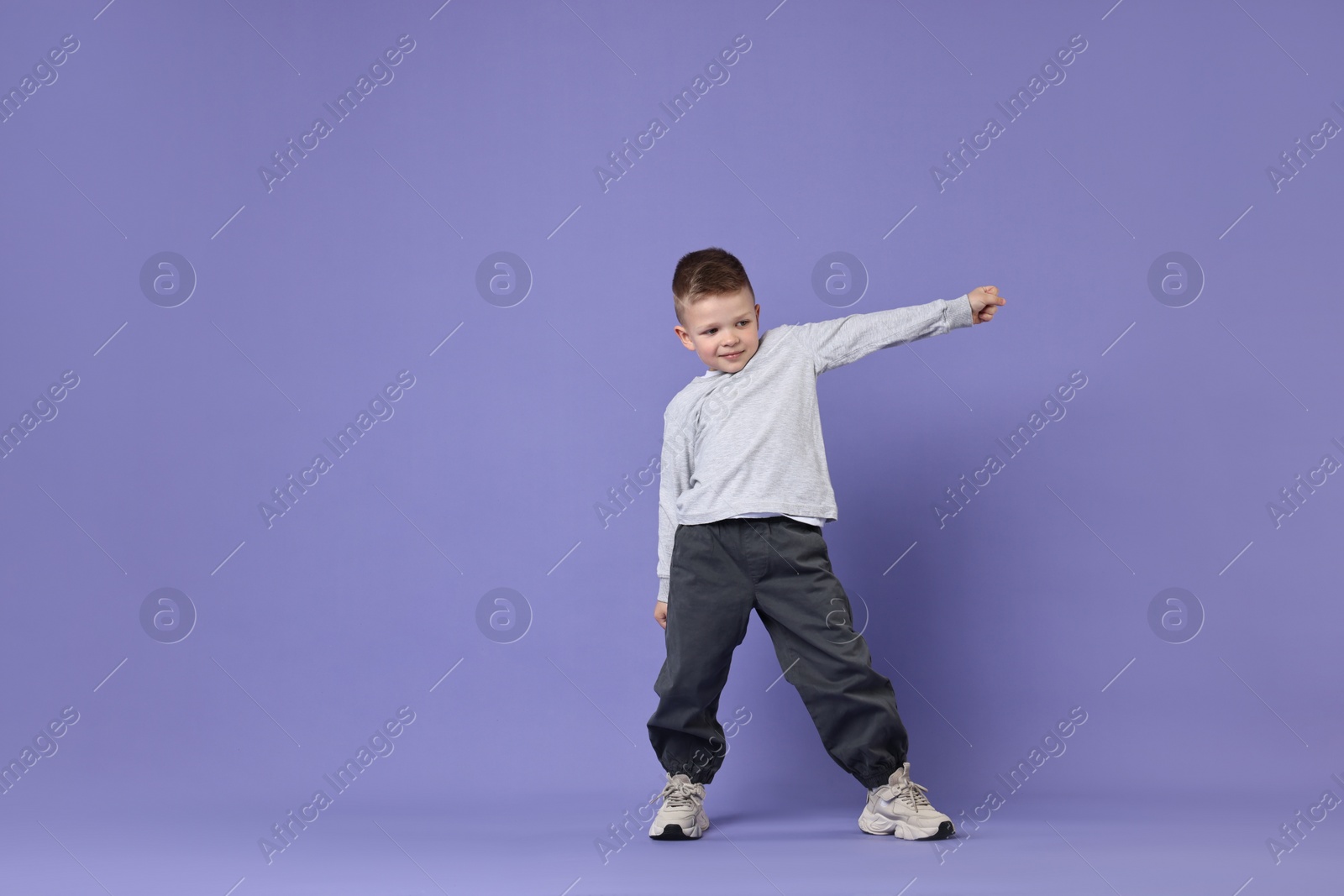 Photo of Happy little boy dancing on violet background. Space for text