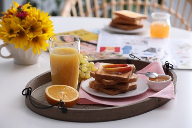 Wooden tray with delicious breakfast and beautiful flowers on white table indoors