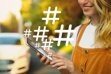 Woman using modern smartphone outdoors, closeup. Hashtag symbols over device