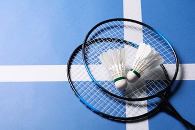 Photo of Feather badminton shuttlecocks and rackets on blue background, top view. Space for text
