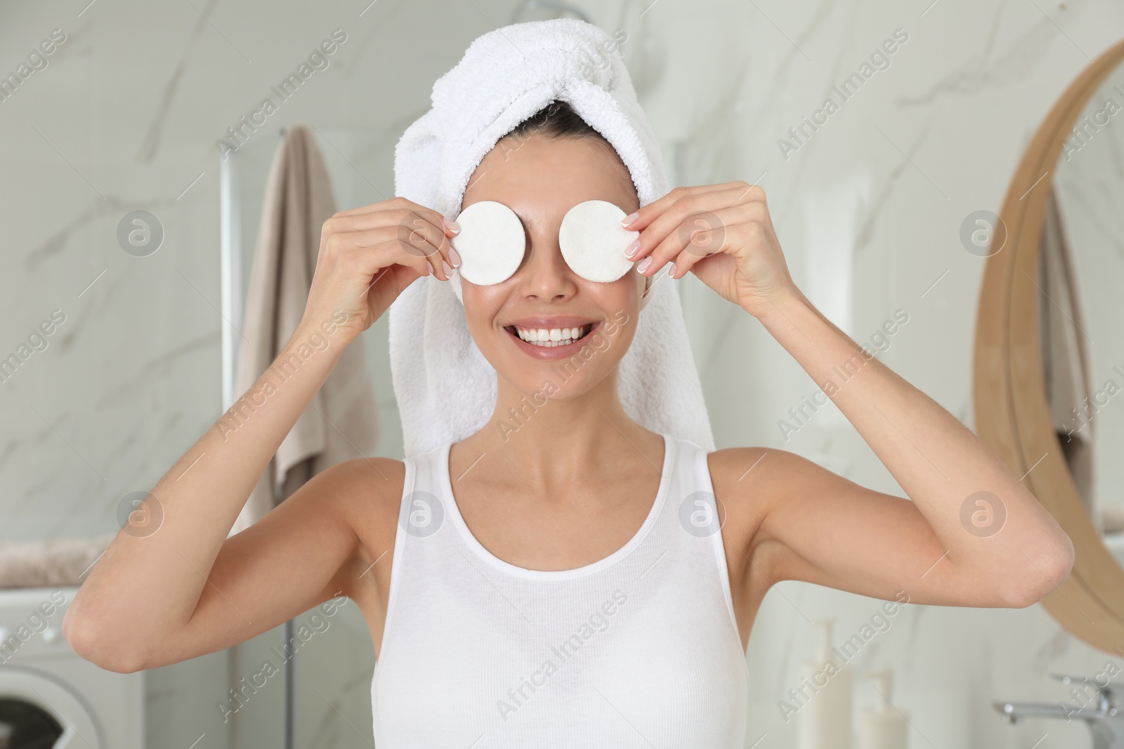 Photo of Happy young woman with cotton pads in bathroom