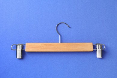 Wooden hanger with clips on blue background, top view