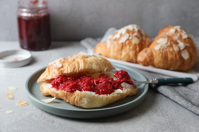 Photo of Delicious croissant with berry jam, butter and spoon on grey table