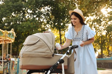 Happy mother with baby in stroller walking in park on sunny day