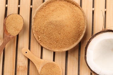 Coconut sugar, spoons, plate and fruit on wooden table, flat lay