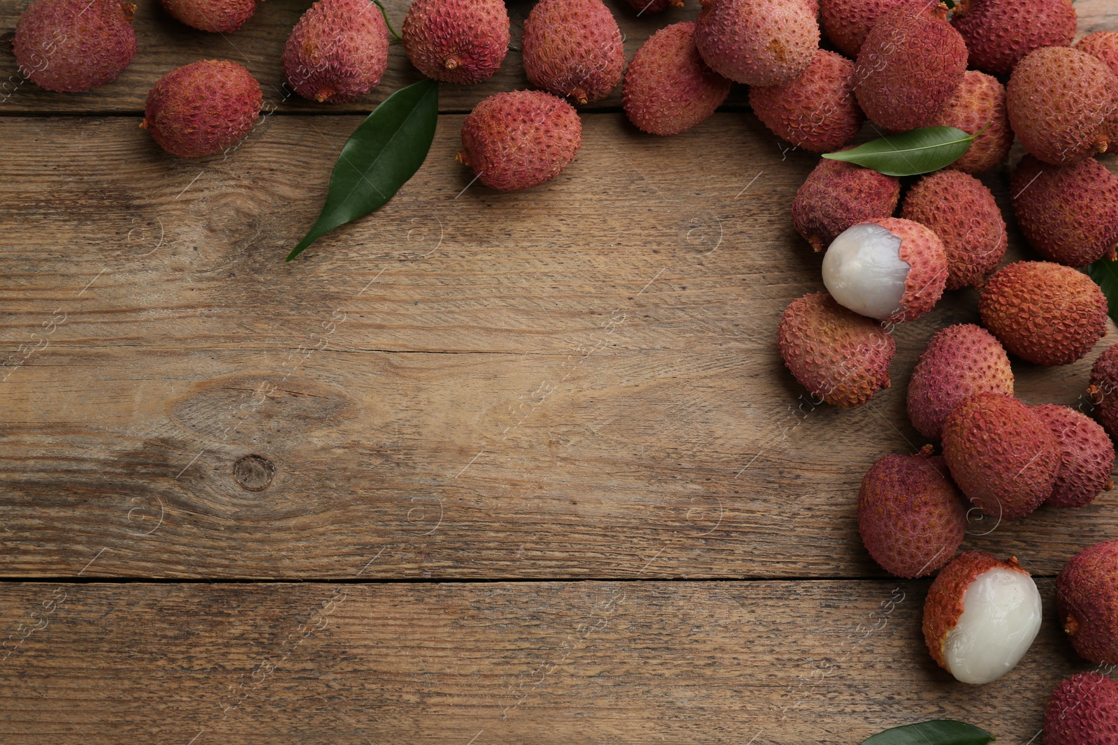 Photo of Fresh ripe lychees with leaves on wooden table, flat lay. Space for text