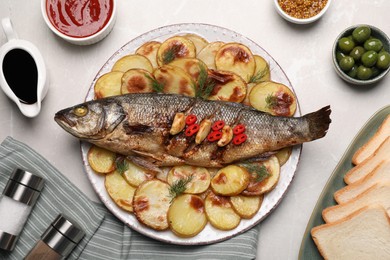 Plate with delicious baked sea bass fish and potatoes on light grey table, flat lay