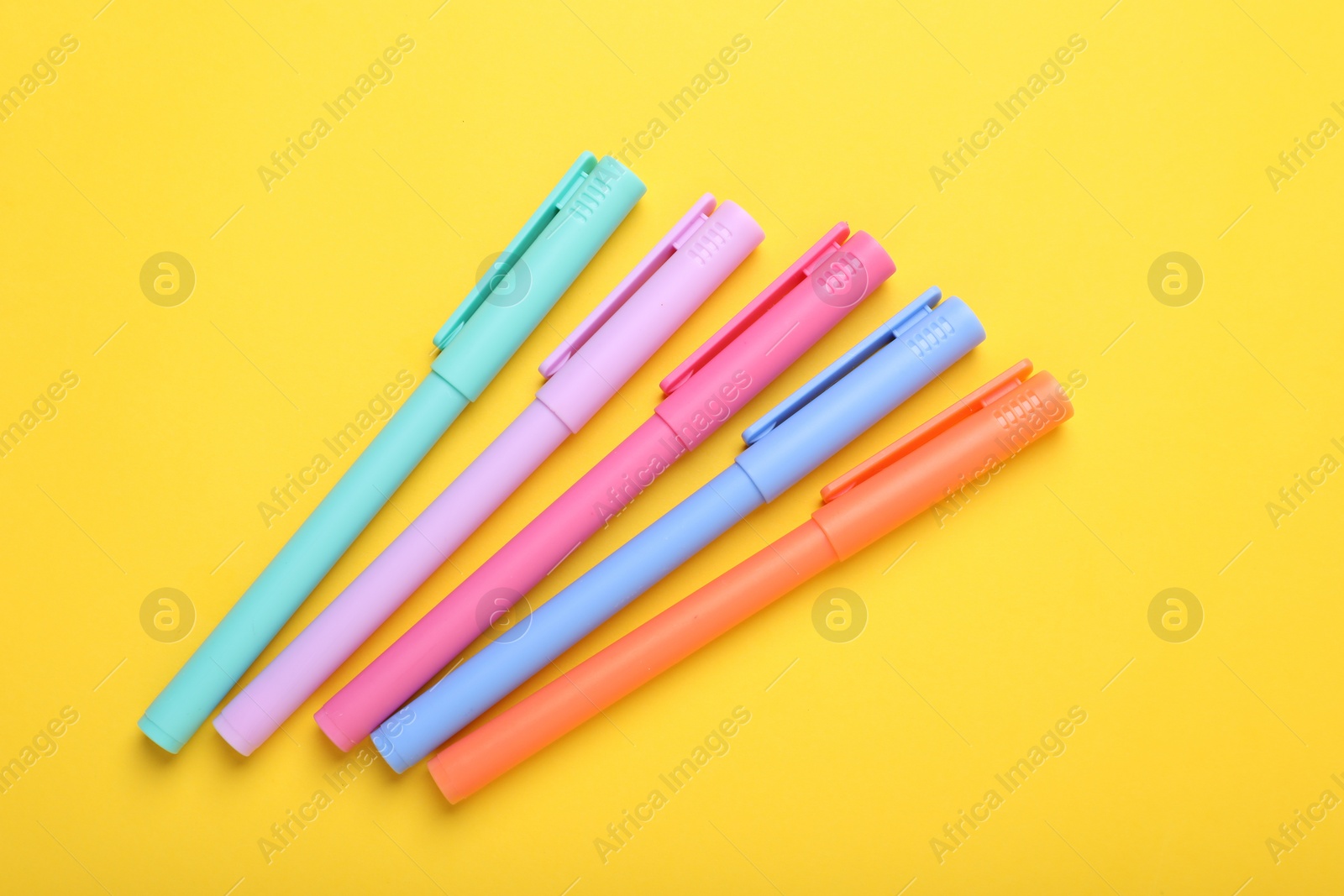 Photo of Many colorful markers on yellow background, above view