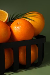 Photo of Fresh oranges in metal basket on green background, closeup