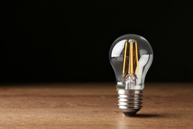 Vintage filament lamp bulb on wooden table against black background. Space for text