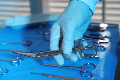 Photo of Doctor taking Pott's scissors from table with different surgical instruments indoors, closeup