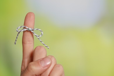 Photo of Woman showing index finger with tied bow as reminder on green blurred background, closeup. Space for text