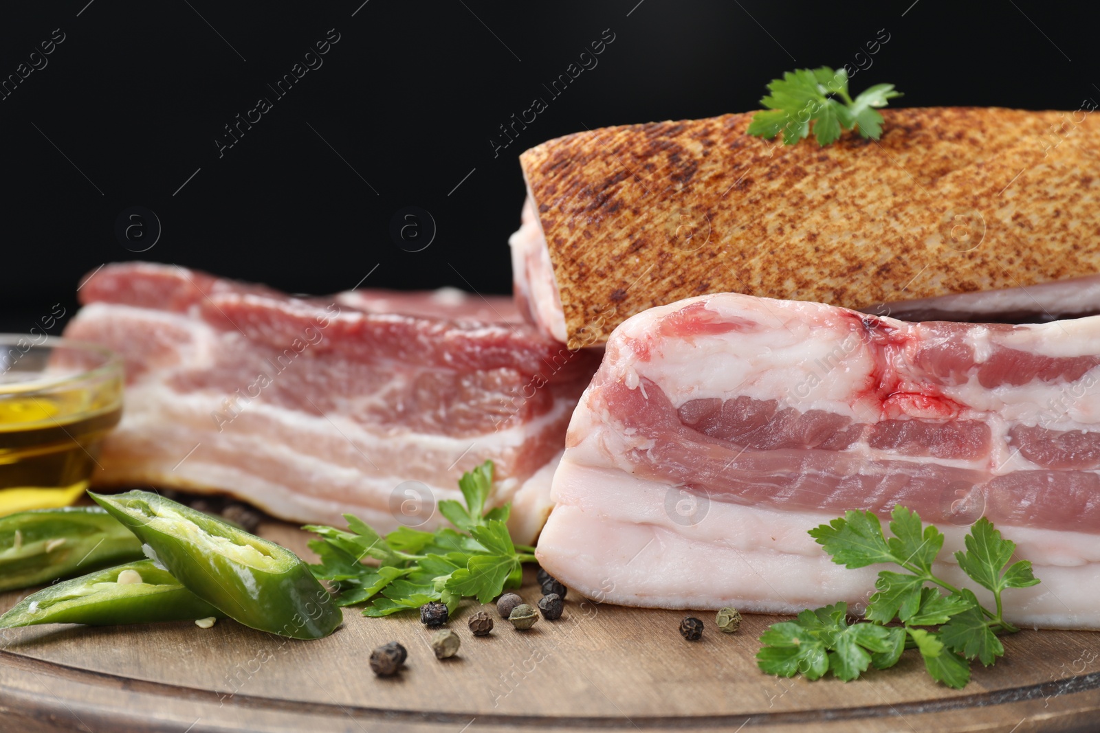 Photo of Pieces of raw pork belly, chili pepper, peppercorns, oil and parsley on wooden board, closeup