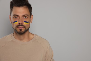 Photo of Man with drawings of Ukrainian flag on face against light grey background. Space for text