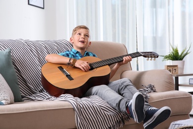 Photo of Cute little boy playing guitar on sofa in room