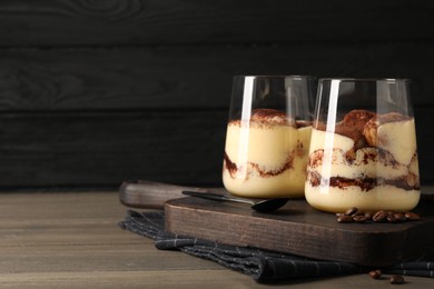 Photo of Delicious tiramisu in glasses, spoon and coffee beans on wooden table. Space for text