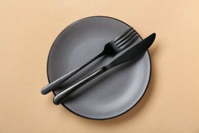 Grey ceramic plate with cutlery on pale orange background, top view