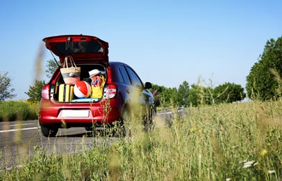 Photo of Family car with open trunk full of luggage on highway. Space for text