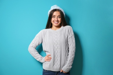 Beautiful young woman in warm sweater with hat on color background