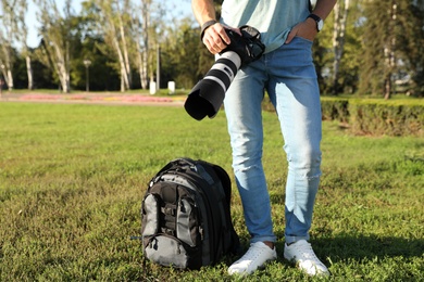 Photo of Young male photographer holding professional camera outdoors