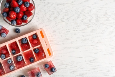 Photo of Flat lay composition with ice cube tray and berries on wooden background. Space for text