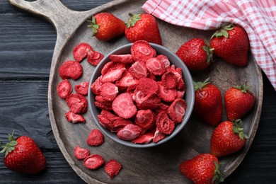 Photo of Freeze dried and fresh strawberries on black wooden table, flat lay