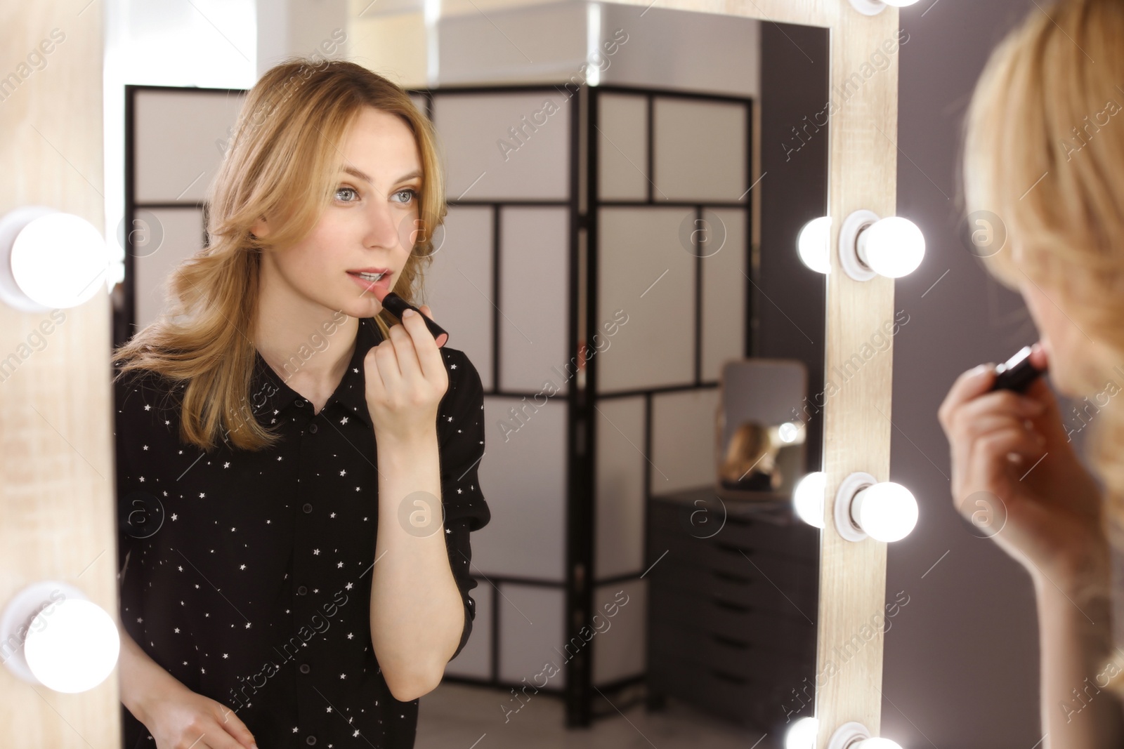 Photo of Young woman applying makeup near mirror in dressing room