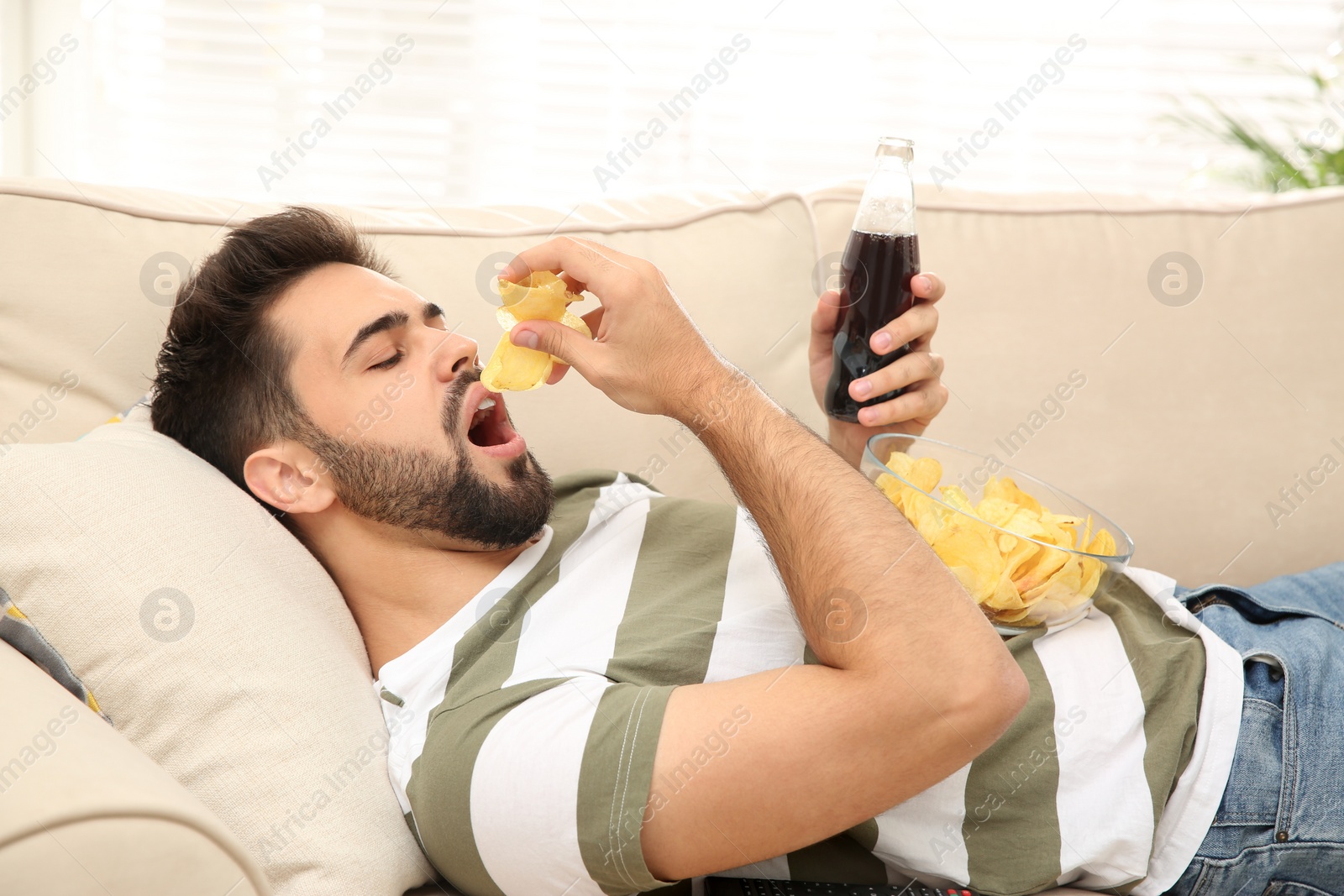 Photo of Lazy young man with chips and drink on sofa at home