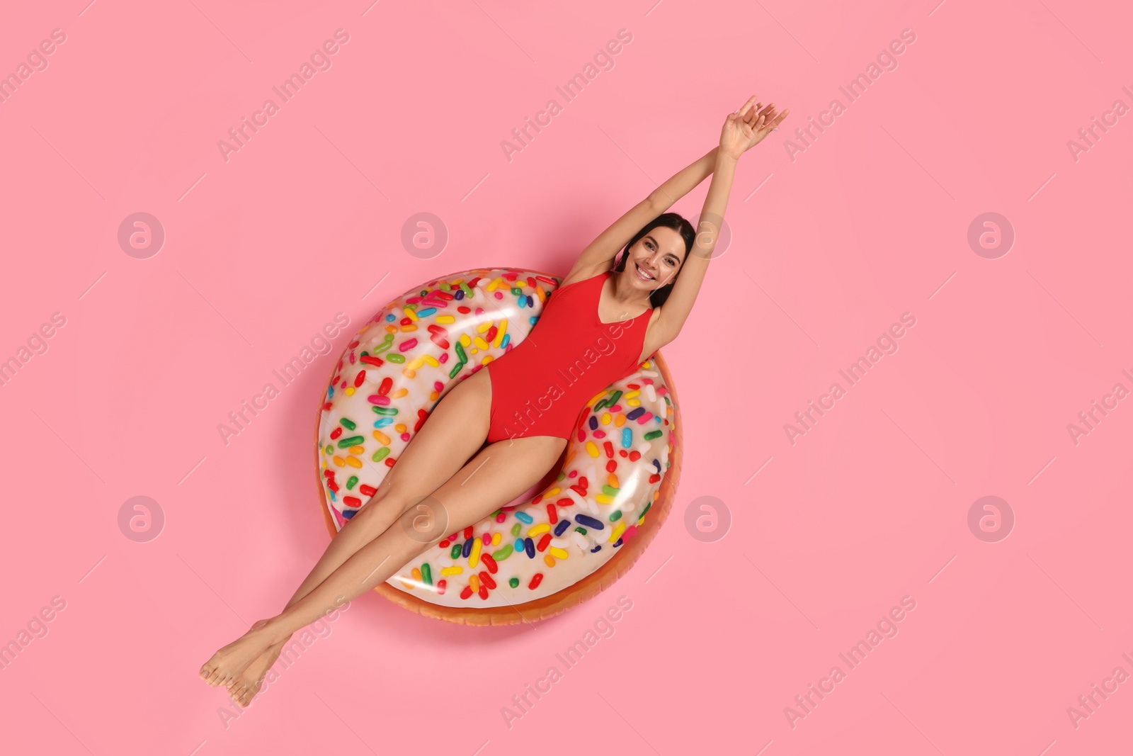 Photo of Young woman in stylish swimsuit on inflatable ring against pink background, top view