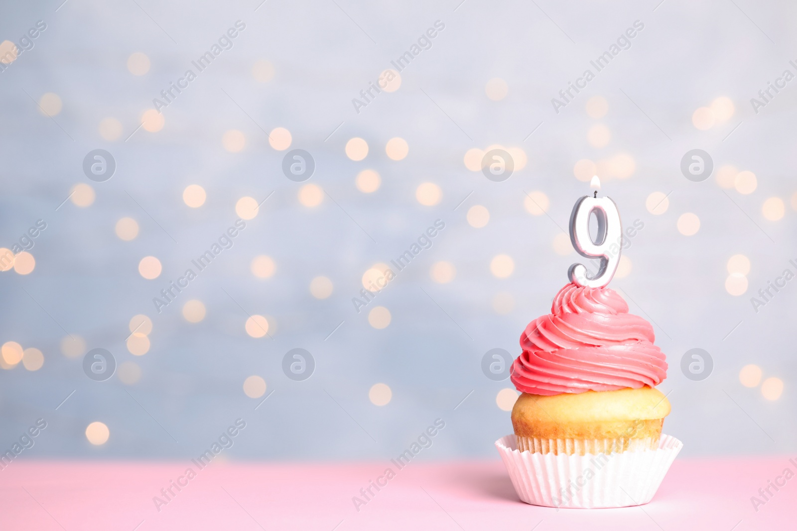 Photo of Birthday cupcake with number nine candle on table against festive lights, space for text