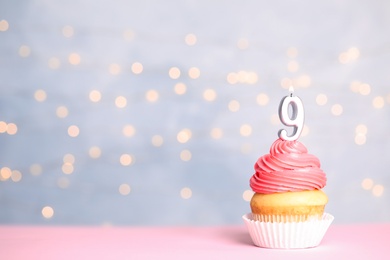 Birthday cupcake with number nine candle on table against festive lights, space for text