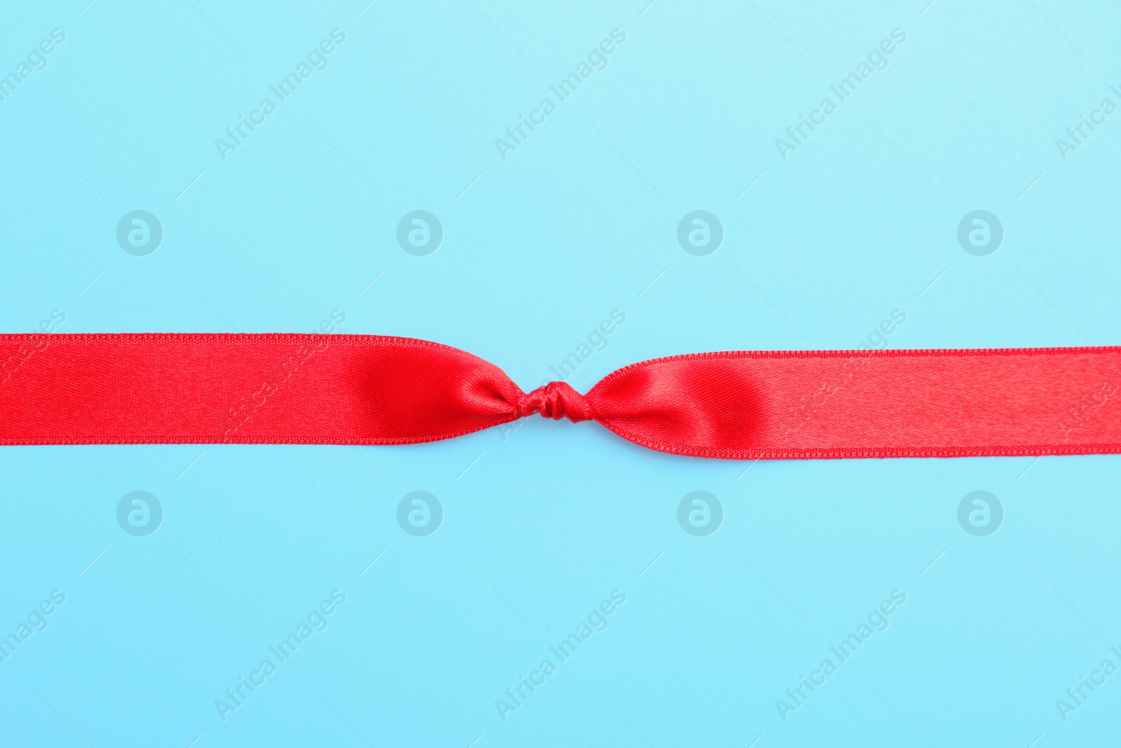 Photo of Red ribbon with knot on color background, top view