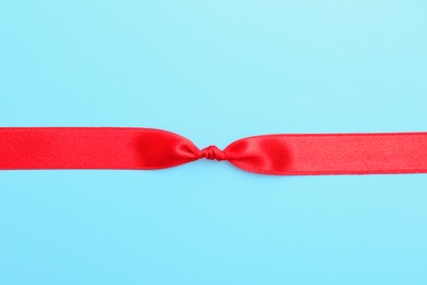 Red ribbon with knot on color background, top view