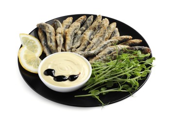 Plate with delicious fried anchovies, lemon slices, microgreens and sauce on white background